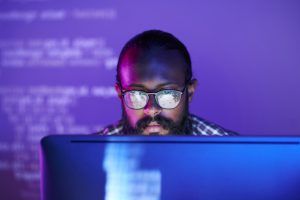 Programador de óculos trabalha em frente a computador em luzes roxas.
